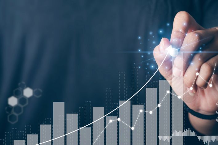 photo of a hand drawing a line that follows and upward trend on a bar graph, indicating growth